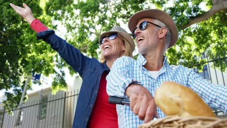 Mature-couple-is-smiling-and-pointing-on-the-same-bike-in-the-street