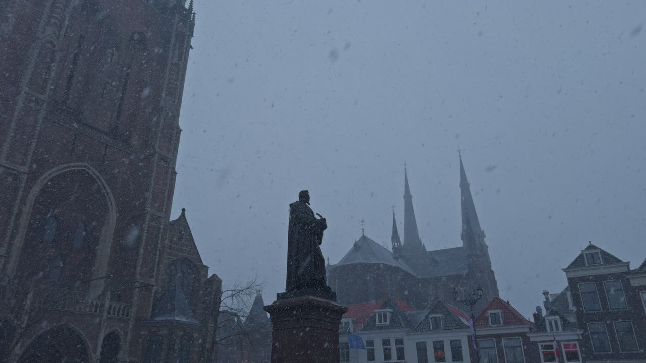 Nevicata invernale in una città olandese in Europa, con edifici dall'architettura tradizionale e una statua in stile europeo, tempo nuvoloso e grigio e un'atmosfera esterna calma
