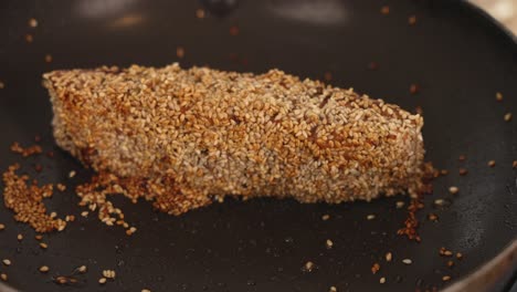 thick cut salmon covered in white sesame seeds, searing the surfaces on saute pan on high heat to produce a flavorful brown crust, slow motion close up shot