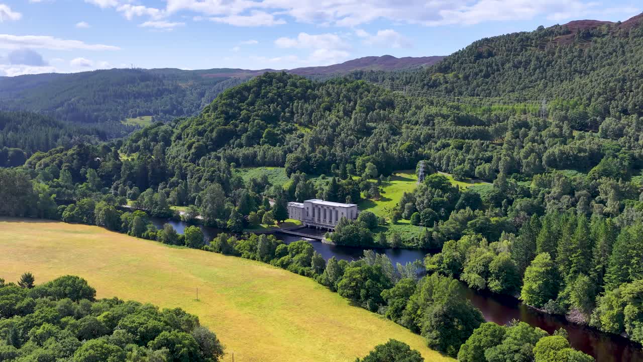 Drone glides over lush highland landscape toward river hydroelectric station under bright daylight