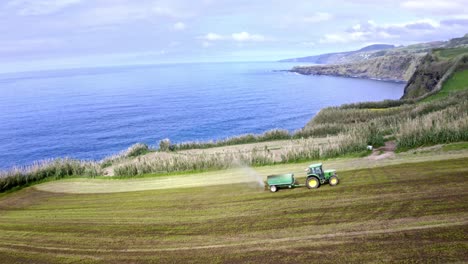 Tractor-with-sowing-trailer-planting-seeds-on-coastal-field,-aerial