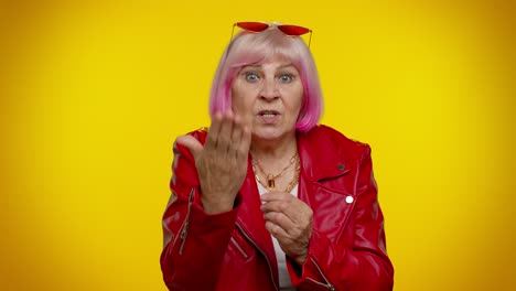 a confident older woman in a red jacket and pink hair poses for a photo.