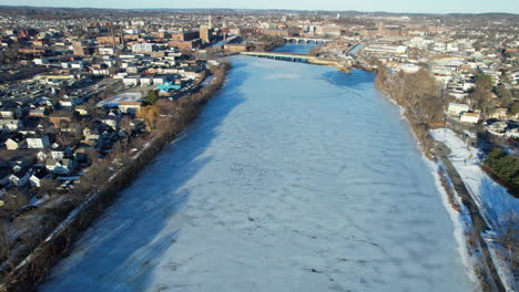 aerial flyover frozen river and downtown of american town in massachusetts. sunny day in quiet american city of lawrence. icy and cold winter day in december. wide shot.