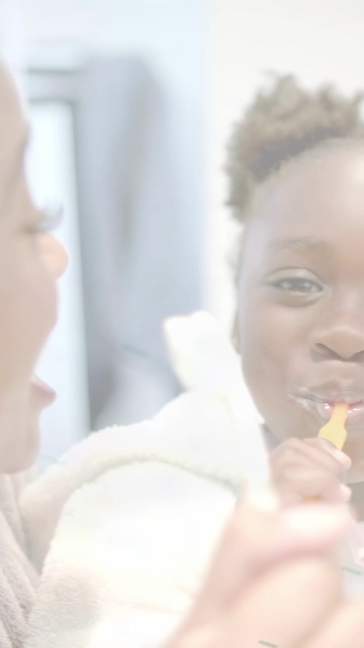 Vertical video: Parent starting brushing, guiding child using brush at mirror, teaching dental care