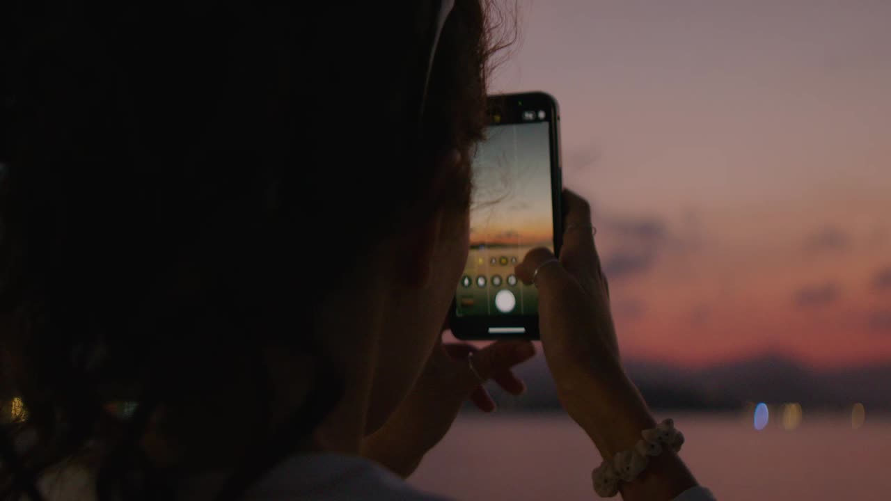 mulher tirando foto do pôr do sol na praia