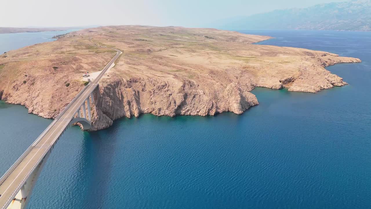 Calm and sunny cinematic drone footage lifting off over the Adriatic Bridge to reveal rich blue waters, dramatic cliffs and the vibrant island of Pag in Croatia.