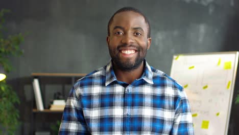 Young-Man-In-Plaid-Shirt-Smiling-Cheerfully-To-Camera-In-The-Office