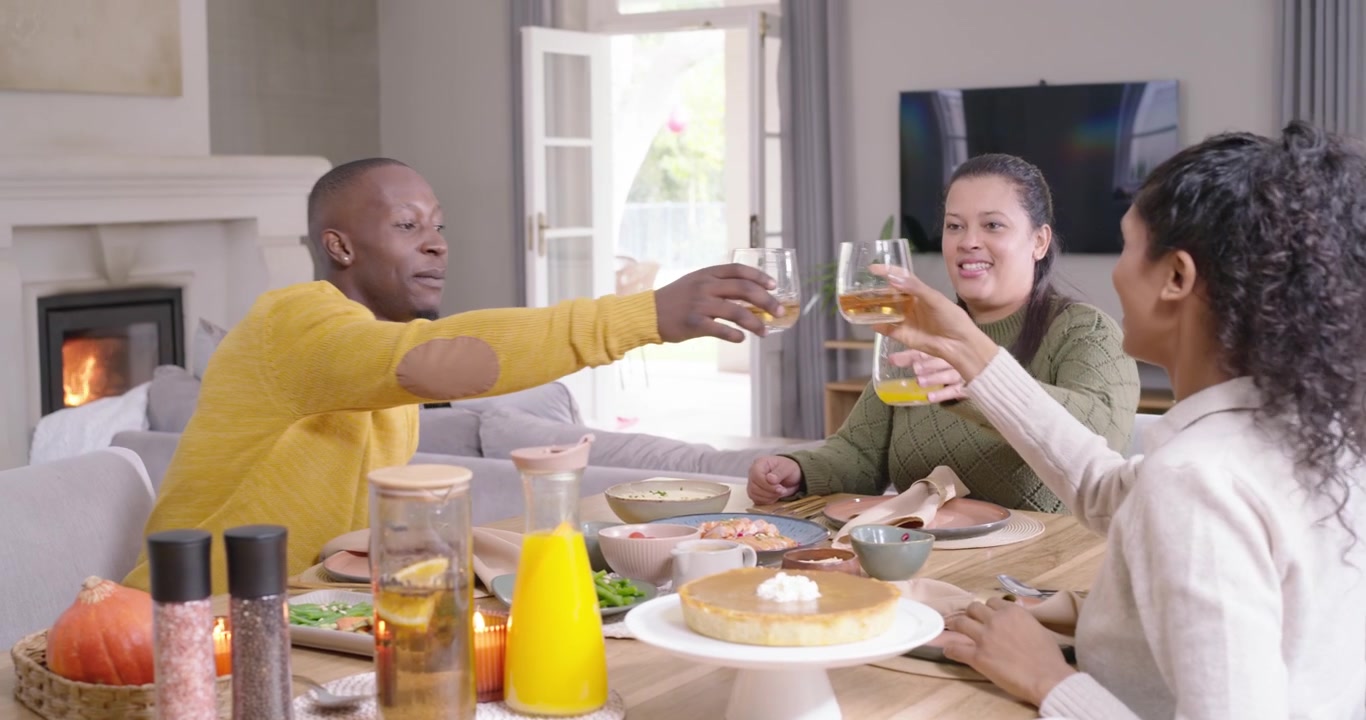 Amici afroamericani che si passano una caraffa, l'uomo con il maglione giallo versa il succo e brinda a tavola.