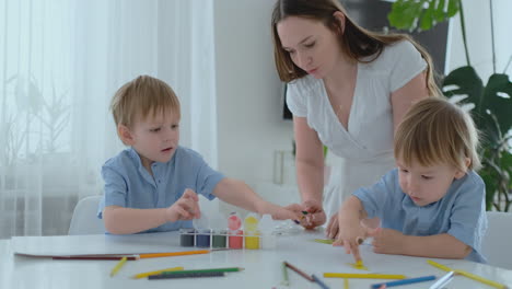 la familia se divierte pintando en el papel con los dedos en la pintura. mamá y dos niños pintan con los dedos en el papel