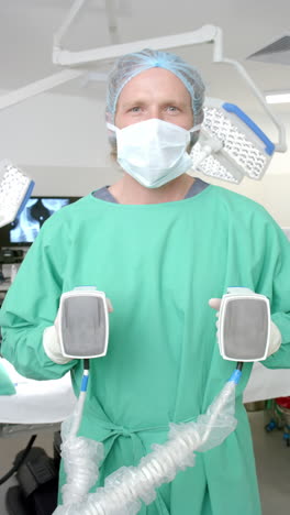 vertical video of portrait of caucasian male surgeon holding defibrillator, slow motion