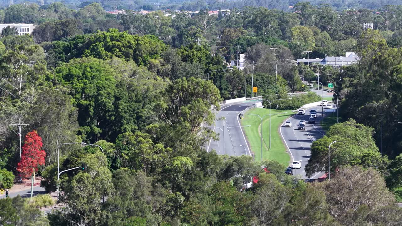 High-angle daytime shot of cars driving along curving tree-lined highway through suburban Australian landscape