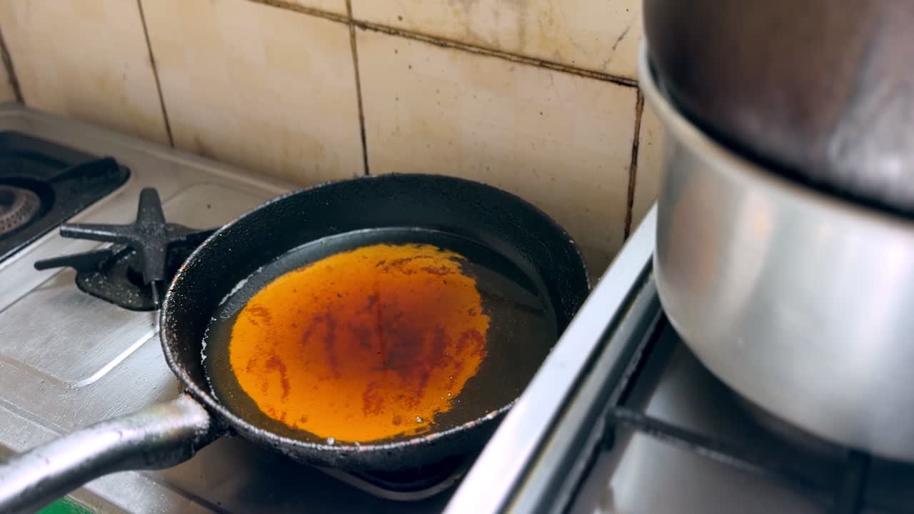 Close-up of a frying pan filled with hot cooking oil heating on a gas stove burner in a home kitchen, showing stovetop cookware and food preparation setup indoors