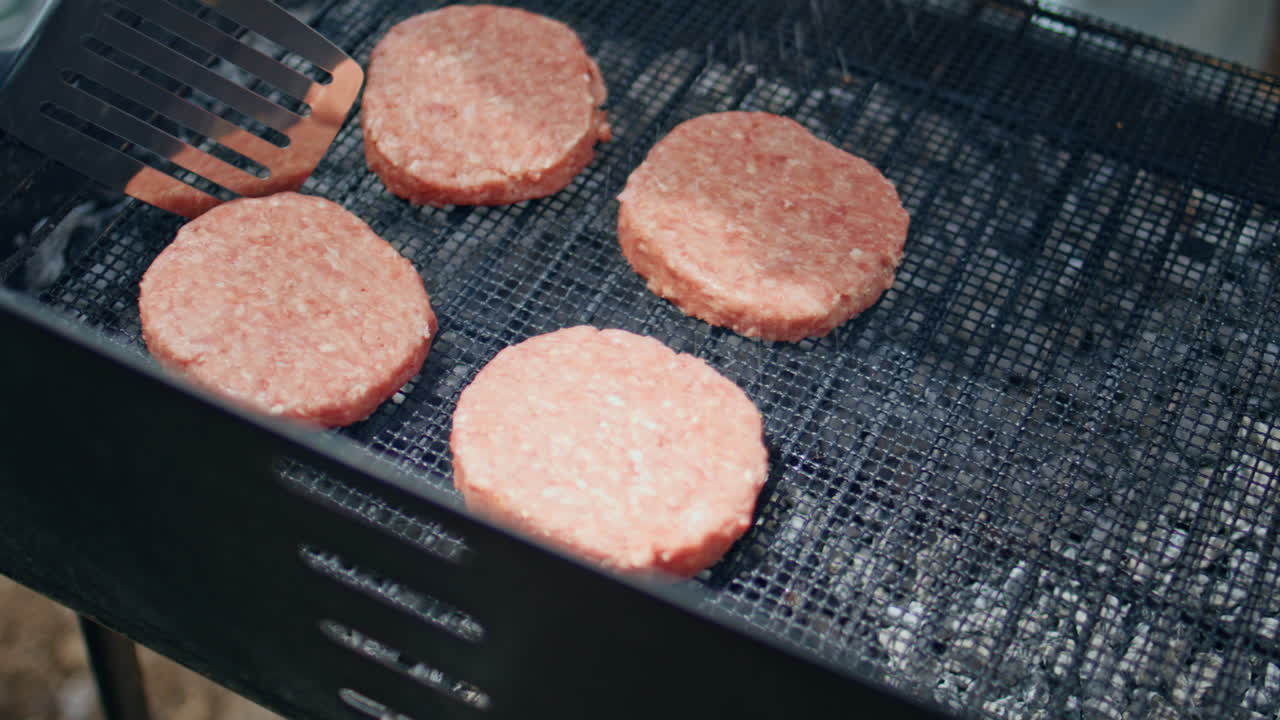 Closeup raw burger patties grilled at forest picnic. Unknown person cooking beef