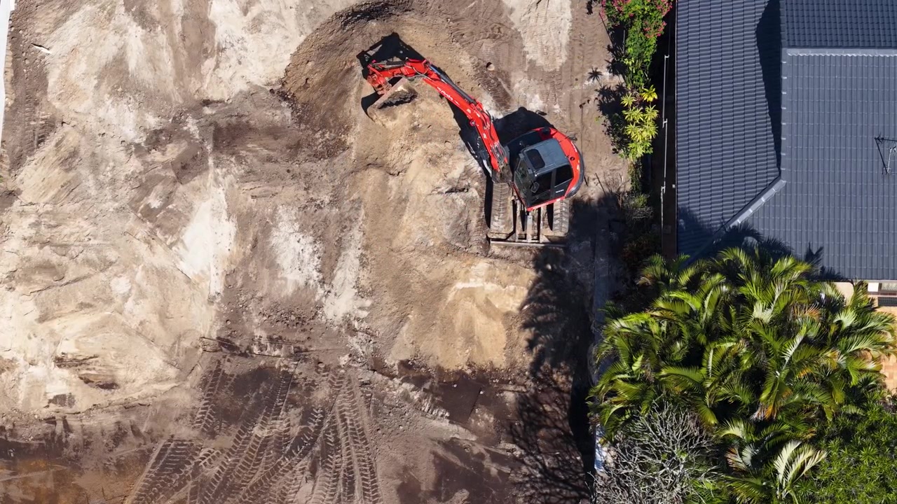 Top-down aerial shot of a red excavator moving soil in a backyard construction zone.