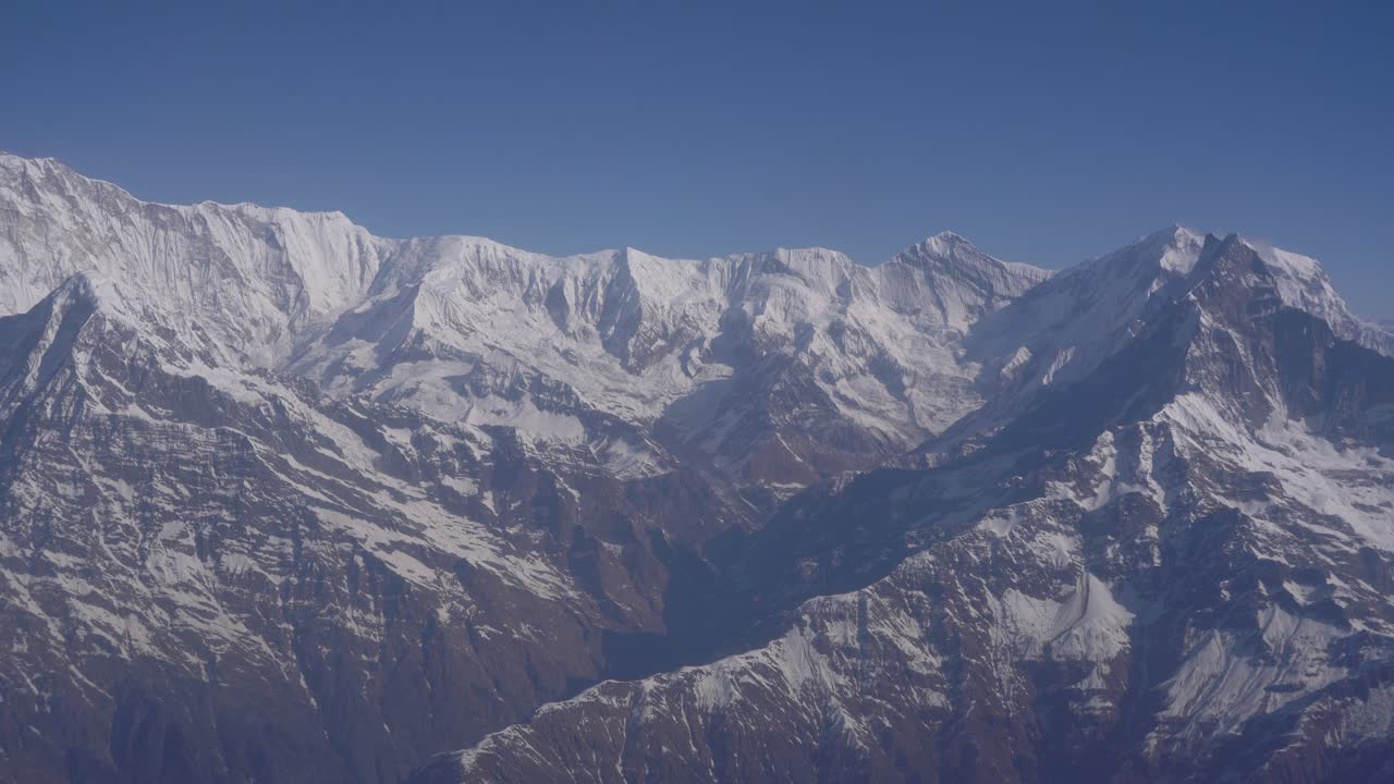 Video of Himalayan peaks from airplane window. Highlights expansive mountain range, cloud layers, and high-altitude environment