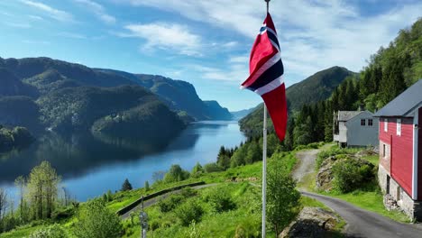 flag moves in wind as drone rises near red barn with veafjord and mountains in bright summer weather