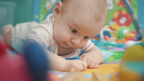 Lovely-baby-looking-yellow-flower.-Close-up-of-child-lying-on-colorful-carpet