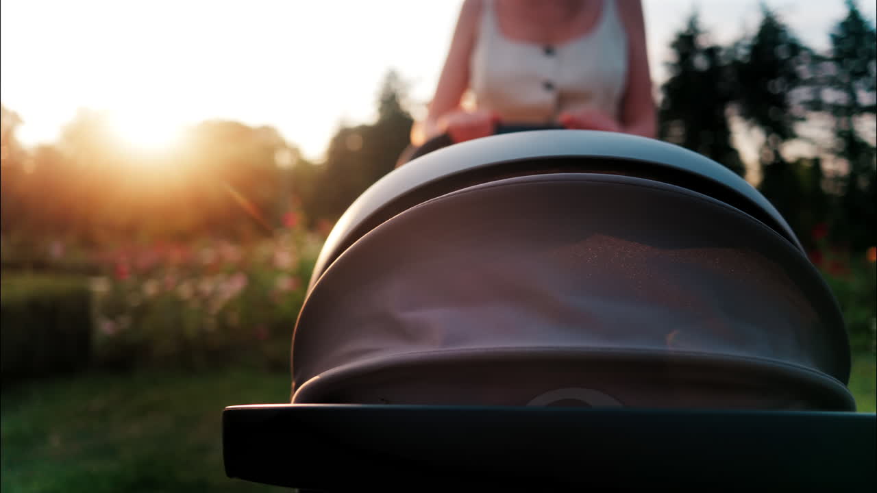 Close up of a stroller being pushed by a mother in the park at sunset