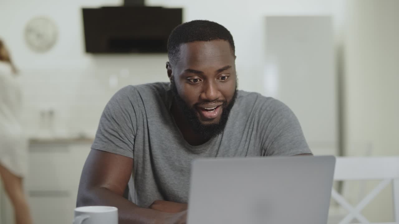 Black man laughing at open kitchen. Red hair woman cleaning kitchen table.