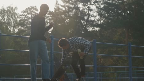 young man with friend in casual clothes practicing skateboarding in skate park