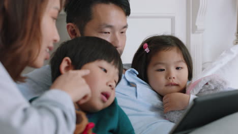 happy asian family using tablet computer at home mother and father with children watching entertainment playing game on touchscreen device learning having fun relaxing in bed 4k footage