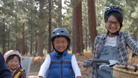 Handheld-pan-of-Asian-family-on-bikes-in-a-forest,-close-up
