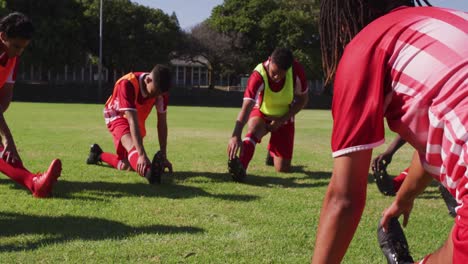 video of diverse group of male football players warming up on field,starching