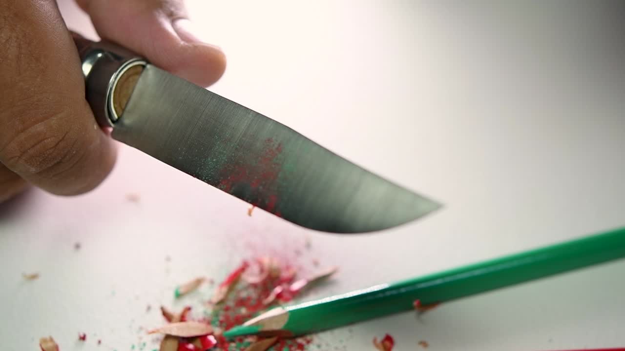 날카로운 칼로 연필과 색연필을 천천히 갈고 있는 손의 영상