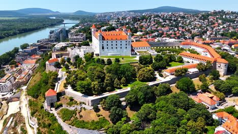 Bratislava Castle surrounded by the lush greenery of the gardens. Drone footage over the rocky waterfront of the Danube in Bratislava, Slovakia