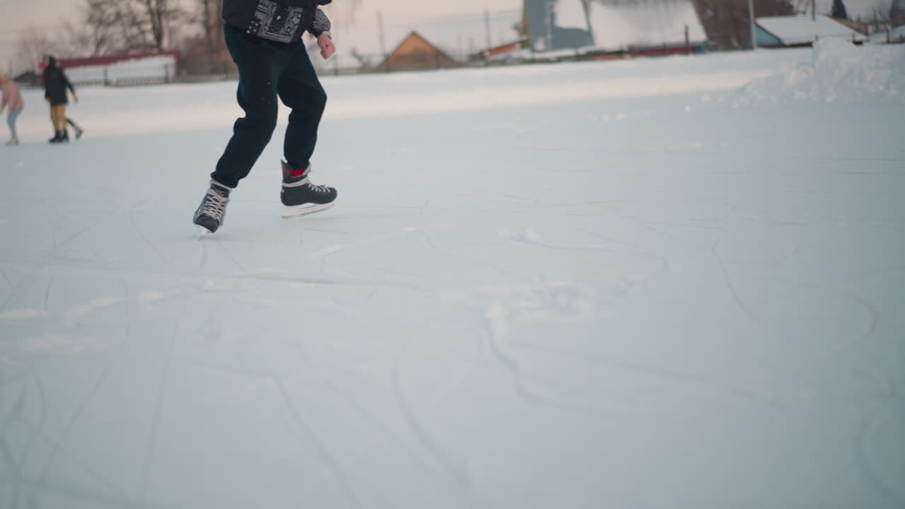 Lower angle view of individual skillfully skating on frozen lake during winter season with other people skating in background near buildings under soft daylight sky
