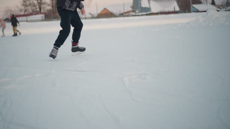 lower angle view of individual skillfully skating on frozen lake during winter season with other people skating in background near buildings under soft daylight sky