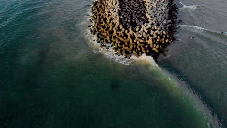 4k aerial fly backward reveal shot of a pier with waves crashing in the early morning during sunrise captured with a drone, pondicherry, india