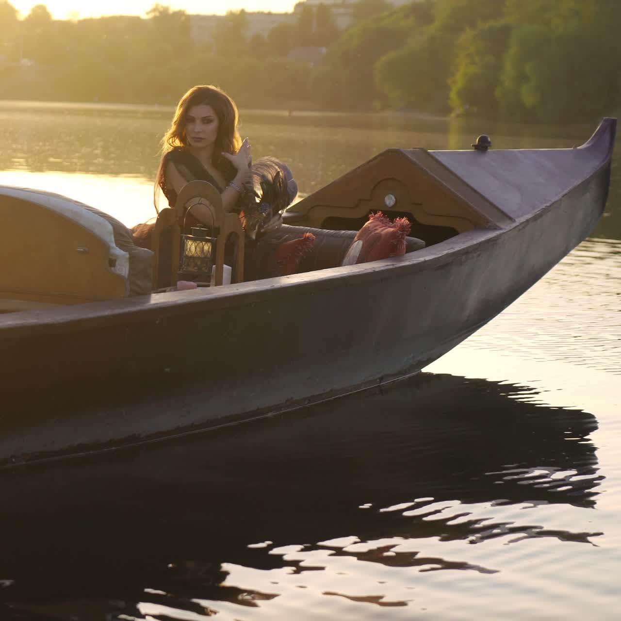A beautiful woman with long hair is sitting in a gondola in an elegant dress at sunset. Carnival in Venice