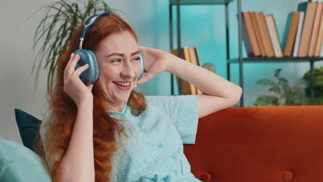 happy young woman in wireless headphones relaxing lying on sofa at home listening favorite music