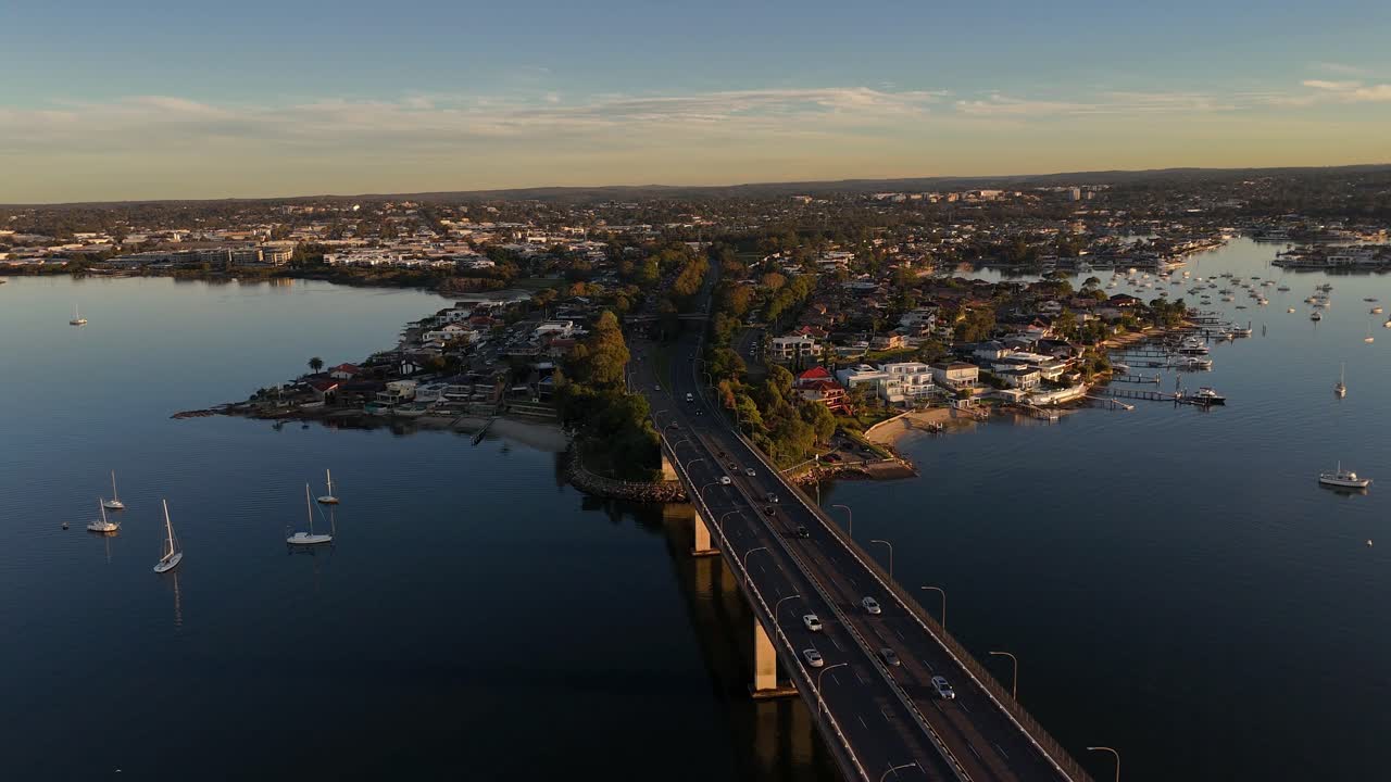 Twilight drone over bridge and harbor at Taren Point with pink reflections on calm water, aerial pullback, Sydney NSW Australia