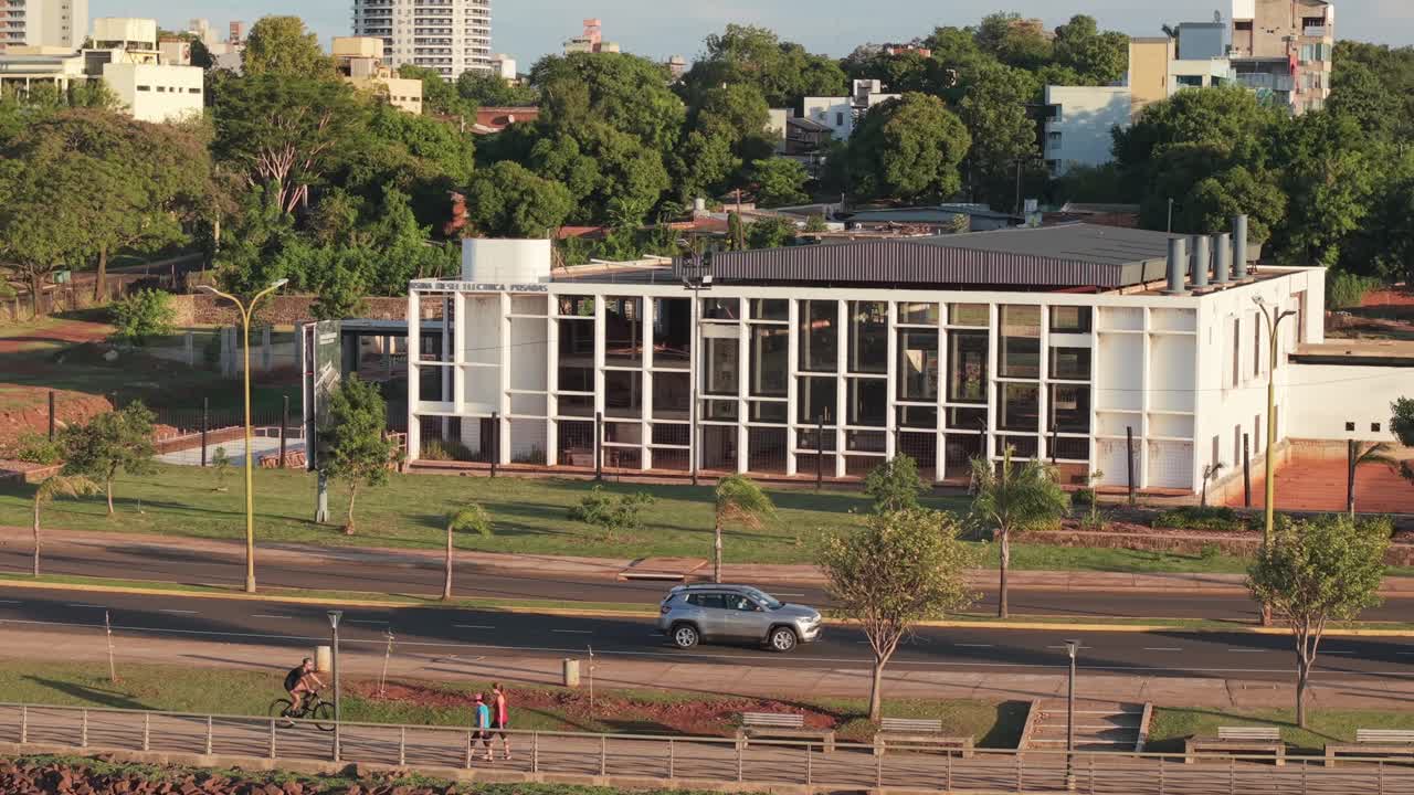 The Usina cultural center in Posadas, Misiones, features a geometric modernist design with white gridded facade, filmed during a slow drone pan with vehicles and trees along the avenue