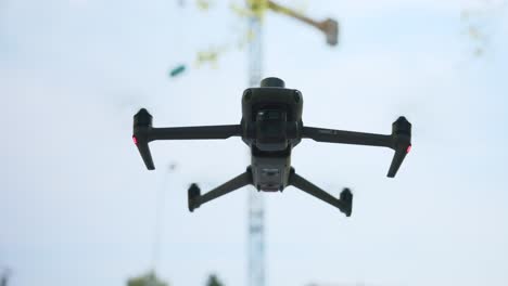 primer plano de un dron cuadricóptero mavic en vuelo estático con una grúa industrial en el fondo