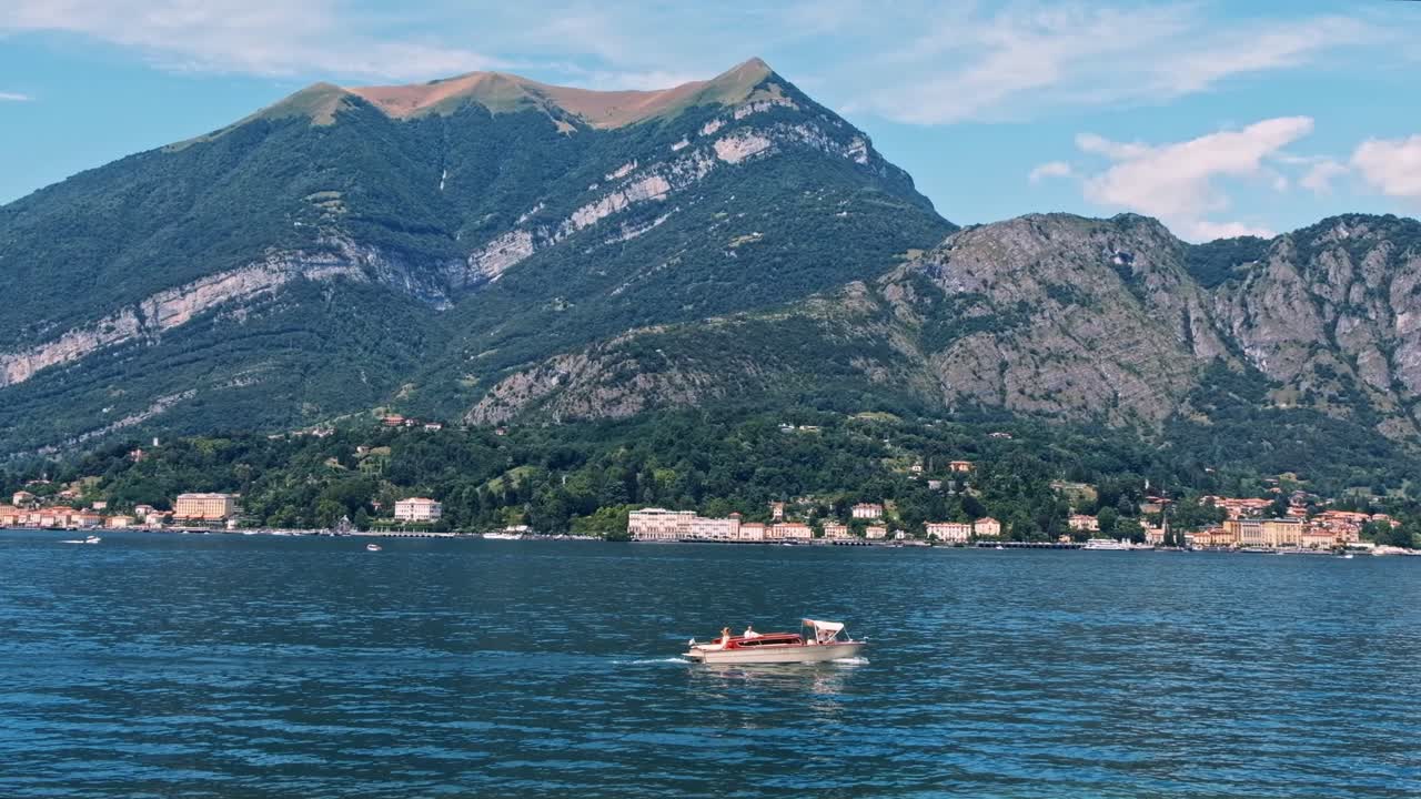 Scenic shot of a boat floating on Como lake near the coastline and mountains in Lombardy, Italy