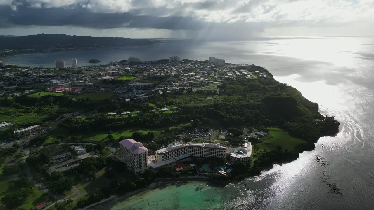 Idyllic orbiting aerial view of coastal resort, hotels, and scenic spots at Oka, Tamuning, Guam during sunset