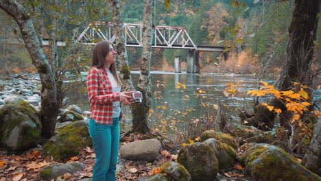 photographer woman walks along riverside among fall colors and takes polaroid