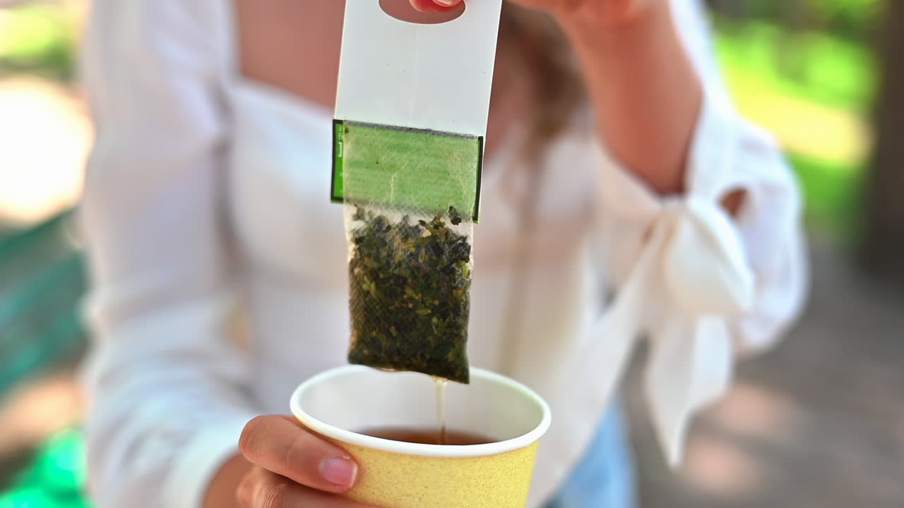 女性が緑茶のティーバッグを紙コップにかき混ぜています。