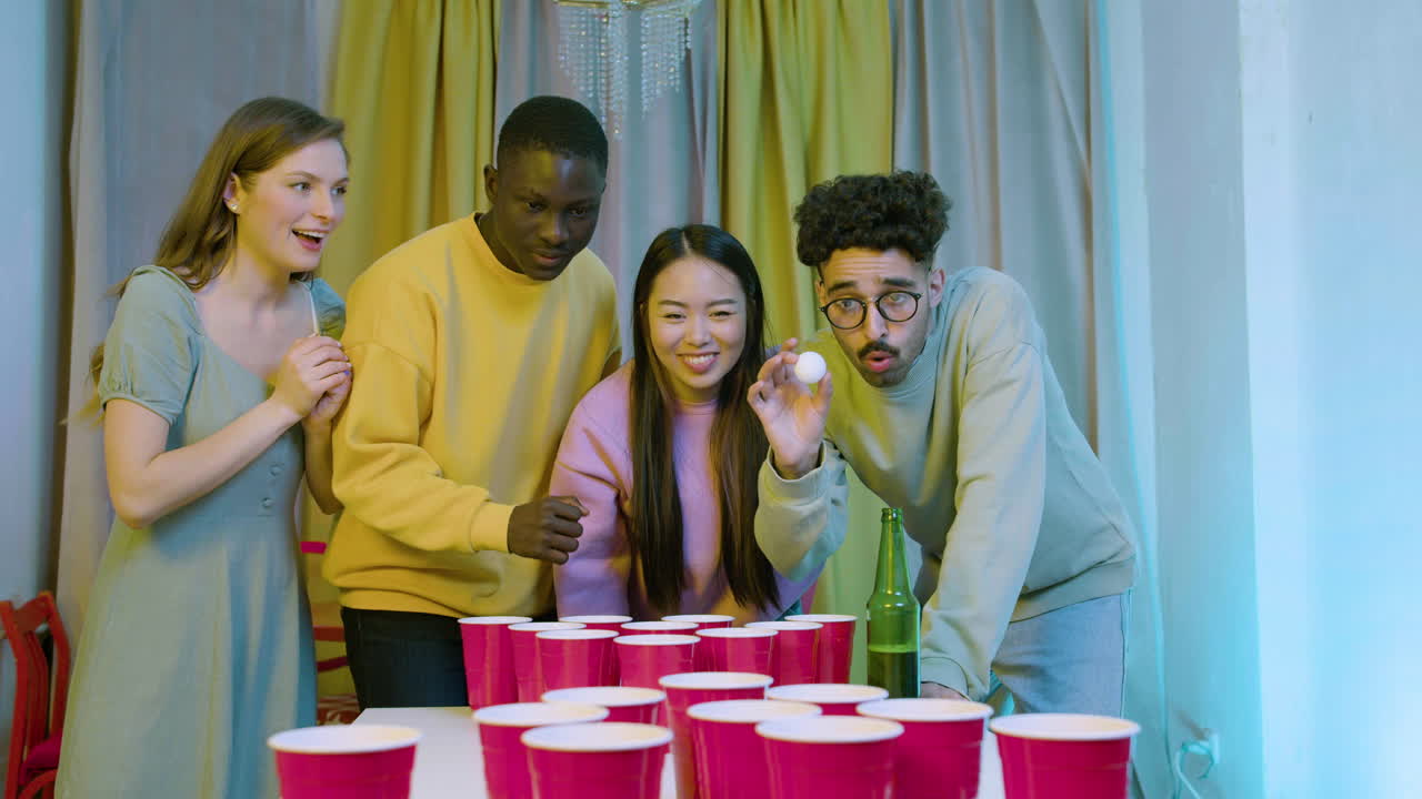 Happy multiethnic young friends playing beer pong at home