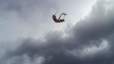 a flying kite with a long tail flying against the ominous clouds in the sky