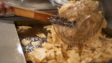 cocinero frito voltea chips de tortilla de maíz con colador de araña en la cocina del restaurante, hd en cámara lenta