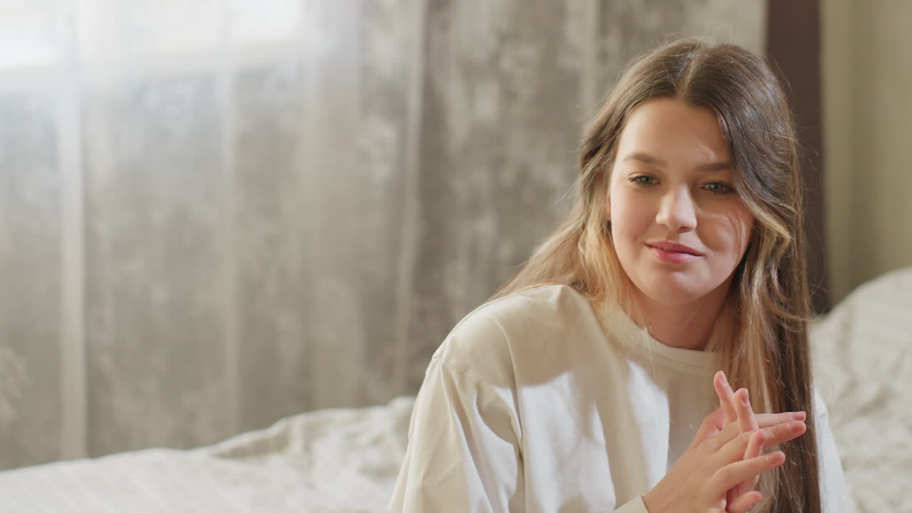 Glad ven med et strålende smil sidder på sengen og snakker varmt med sin ledsager. Ekspressive håndbevægelser giver livlighed, og en hyggelig soveværelsesbaggrund fremhæver det oprigtige, venlige øjeblik.