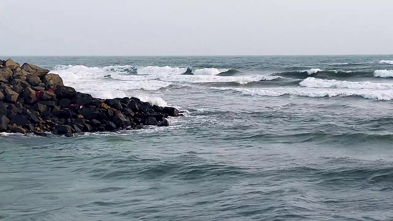 Onde potenti che si infrangono contro scure rocce frangiflutti di basalto sulla costa di Dwarka. Perfetto per progetti documentaristici su tempeste, potenza dell'oceano, India costiera, pellegrinaggi e paesaggi marini drammatici