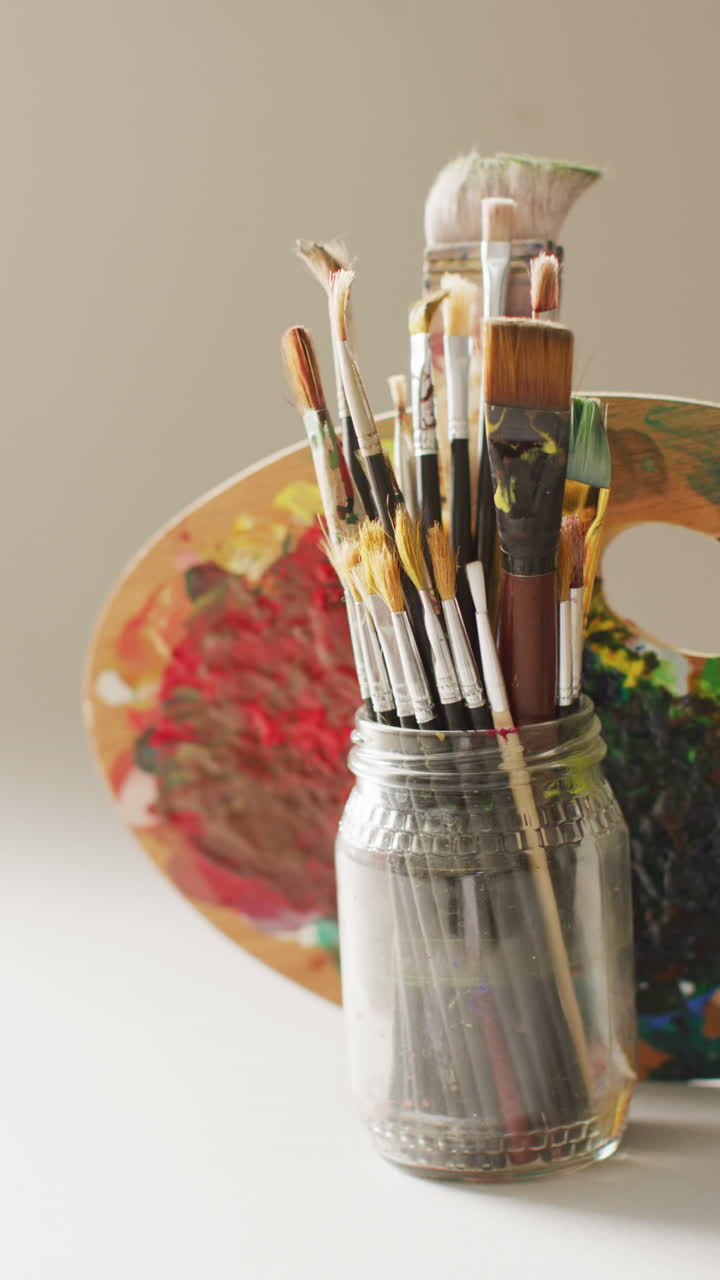 video vertical de pinceles en un frasco y paleta utilizada en fondo gris con espacio de copia