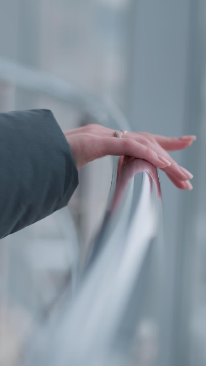 Close-up of lady's hand with ring placed on rail as she walks, with modern building glass in background, giving a stylish, contemporary feel in an urban setting
