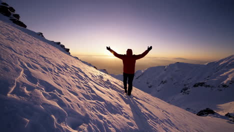 man celebrating sunrise on snowy mountain