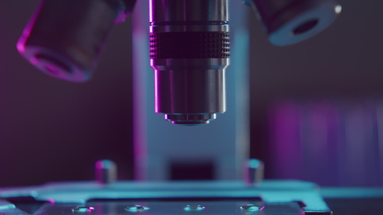 Close Up of Microscope Lens Approaching Glass Slide with Sample in Lab